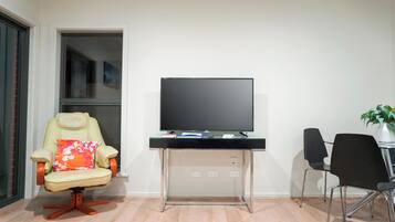 A modern living room with a beige armchair with a floral cushion, a black desk with a flat-screen TV, and two black chairs.