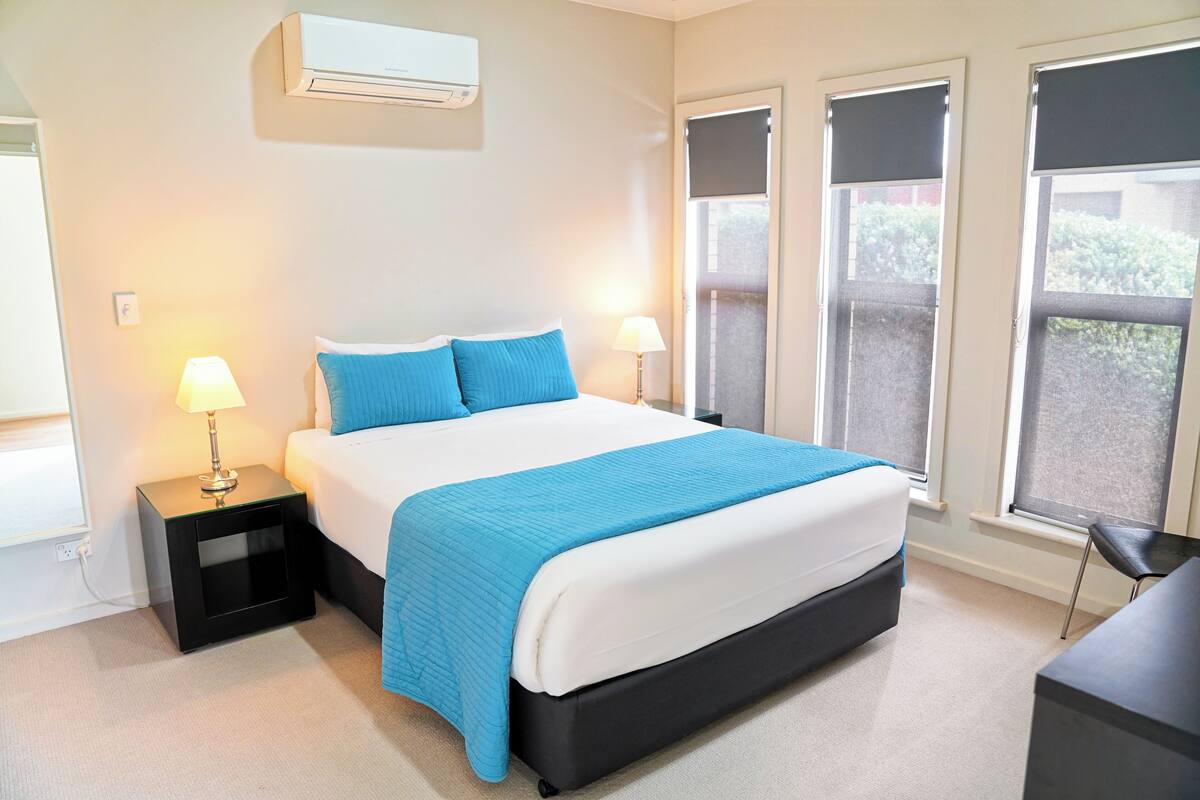 Een slaapkamer met een bed, twee nachtkastjes met lampen, een raam met uitzicht en een airconditioning.