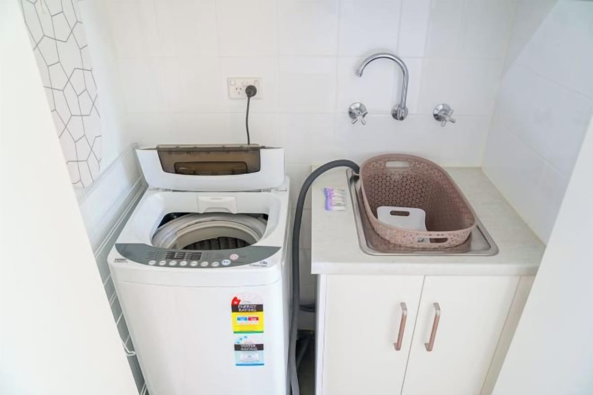 Un lavadero pequeño con lavadora, tendedero y lavabo con cesto.