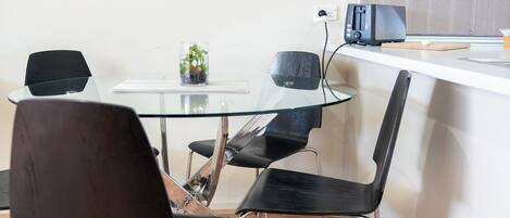 A modern kitchen with a glass table, black chairs, and a small plant.