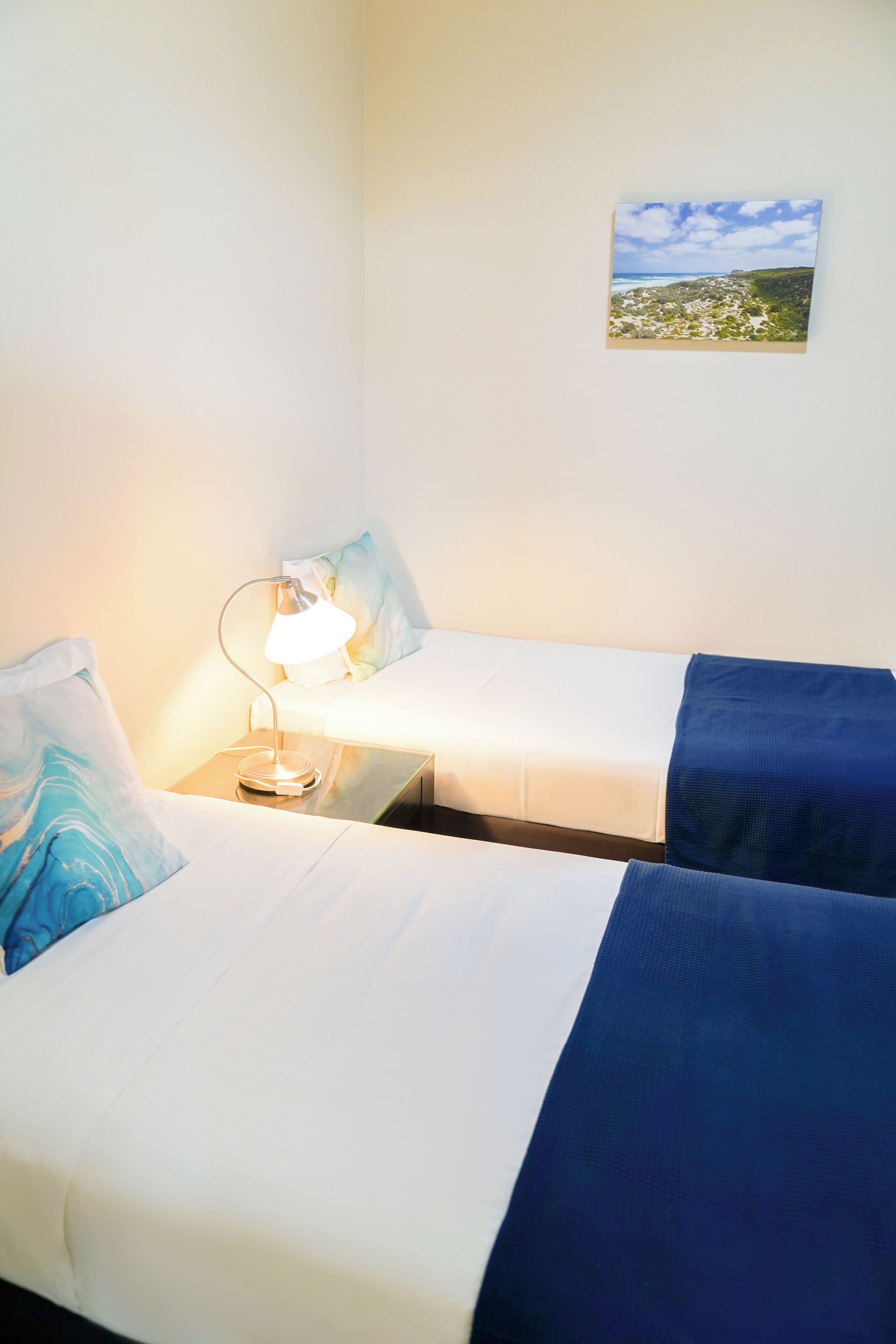 Une chambre d’hôtel avec deux lits simples, une table de chevet avec une lampe et un tableau au mur.
