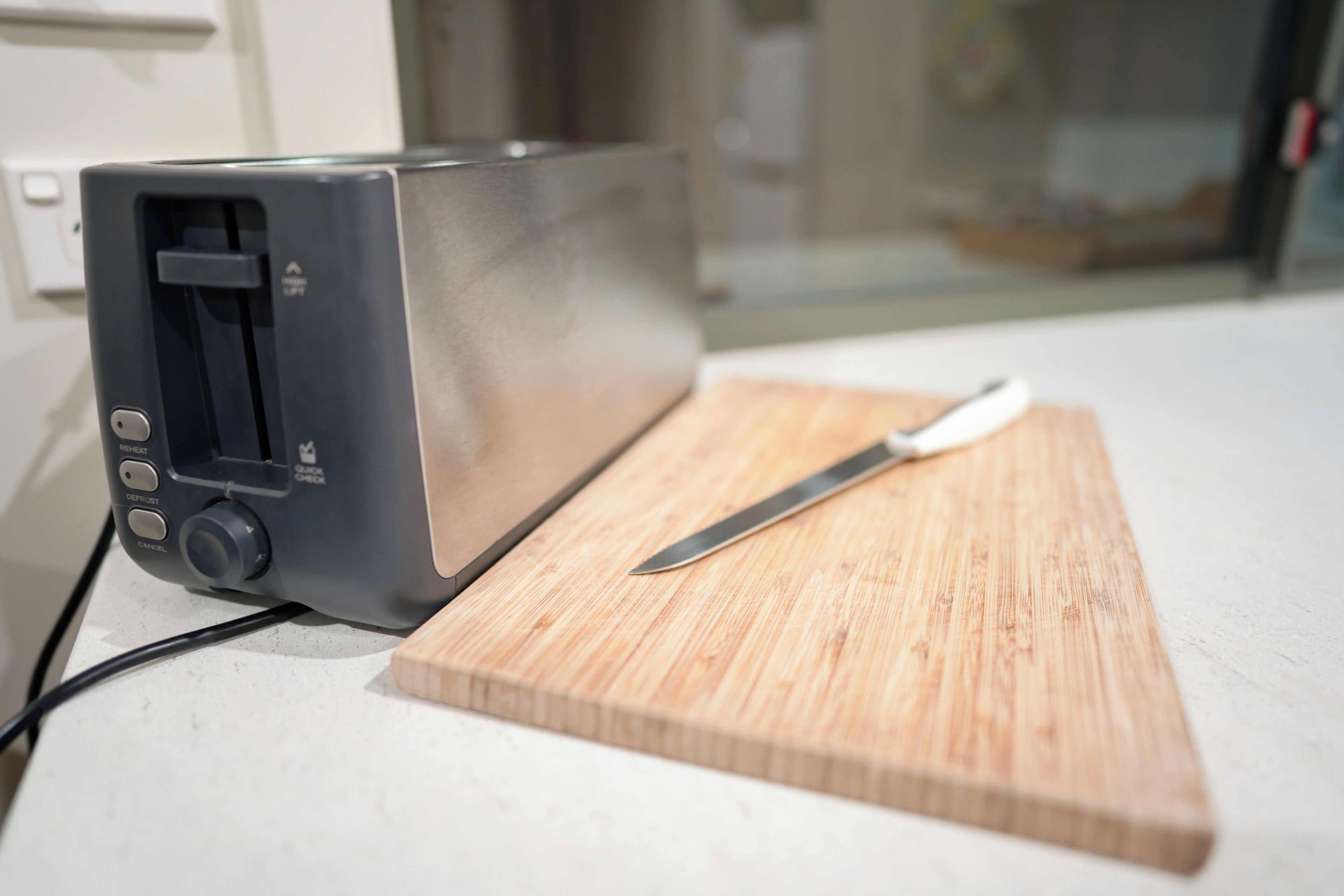 A toaster on a kitchen counter with a wooden cutting board and a knife.