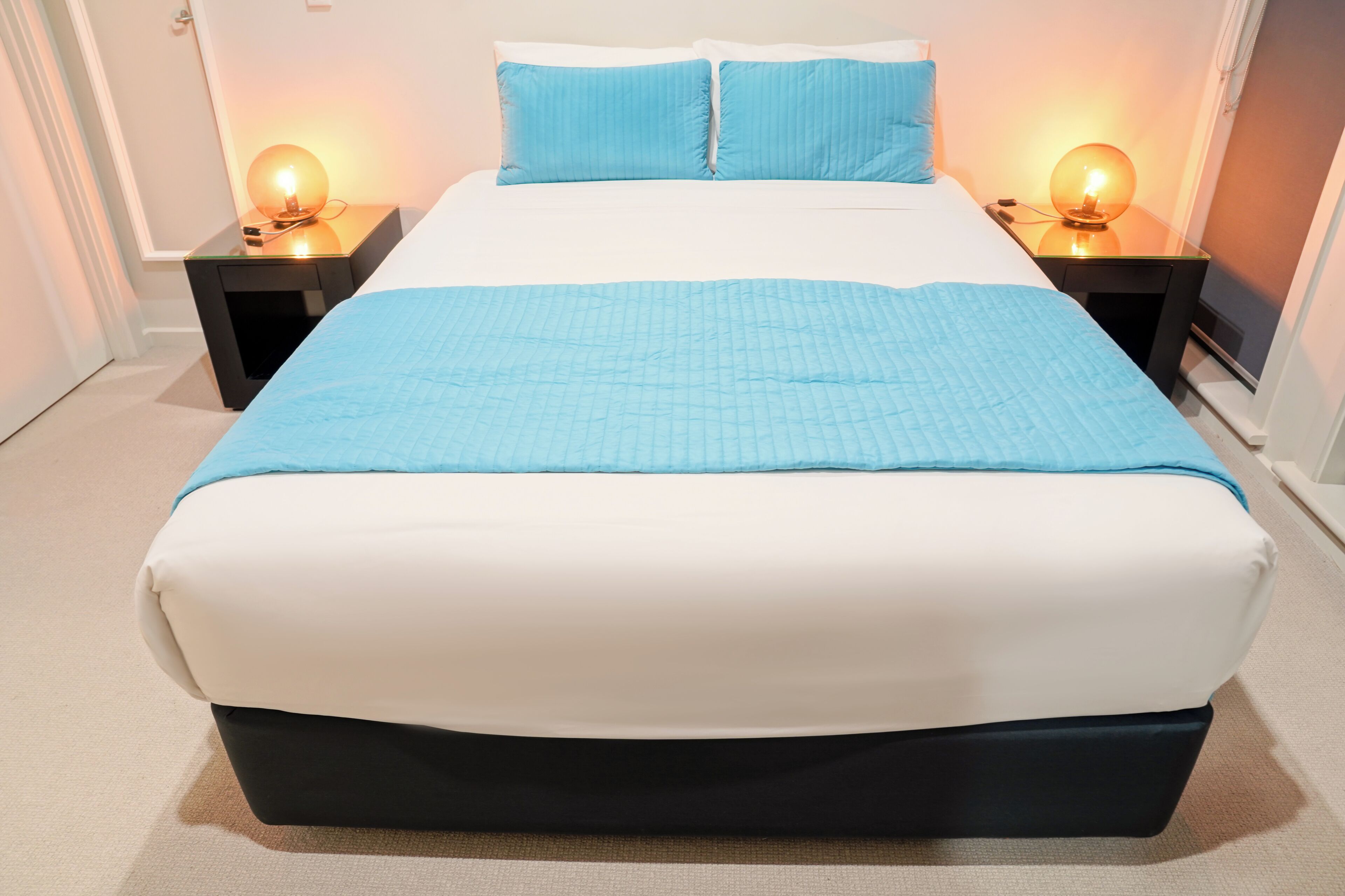 A bed with a blue quilt, white pillows, and two bedside lamps.