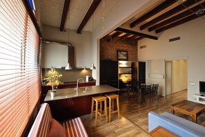 A modern kitchen with a central island, wooden stools, and a dining area with a table and chairs. - Gracia Terrace Design (Barcelona)