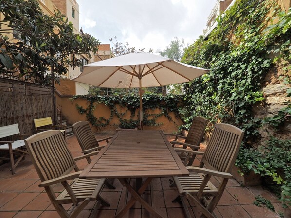 A patio with a wooden table and four chairs, an umbrella, and a wall covered in ivy. - Gracia Terrace Design (Barcelona)