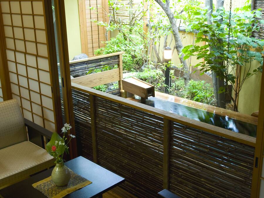 A traditional Japanese-style room with tatami flooring, a low table with a vase, and a view of a garden through a shoji screen.