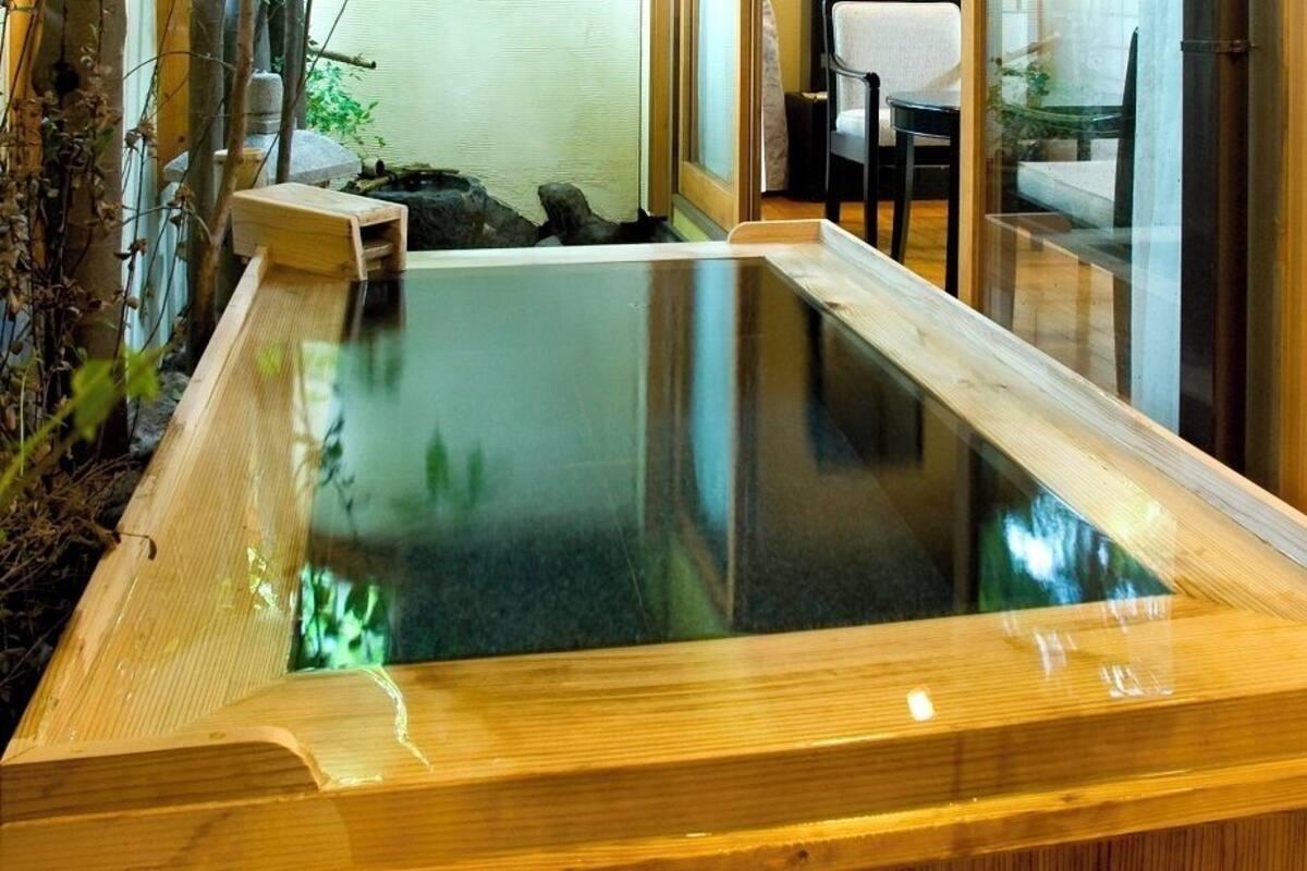 A wooden hot tub with a glass top, surrounded by plants and a chair.