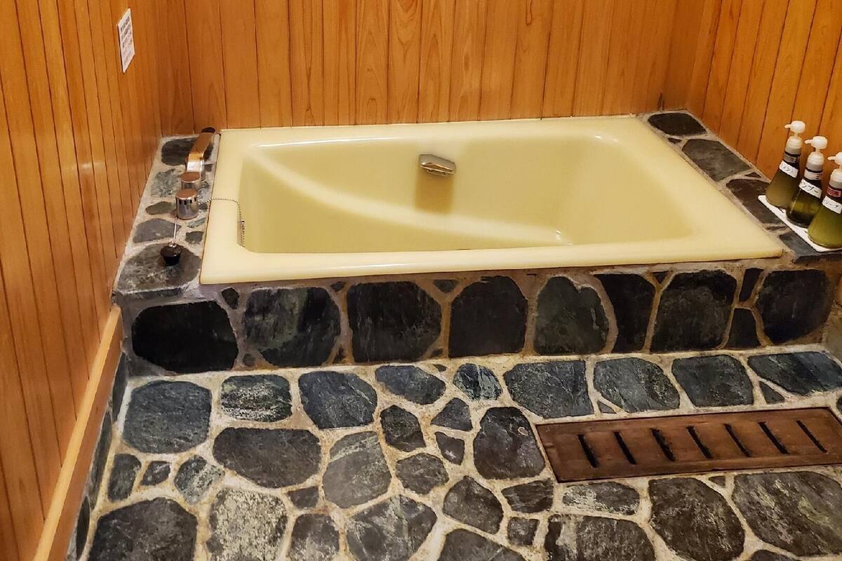 A stone-floored bathtub with a wooden wall and a drain.