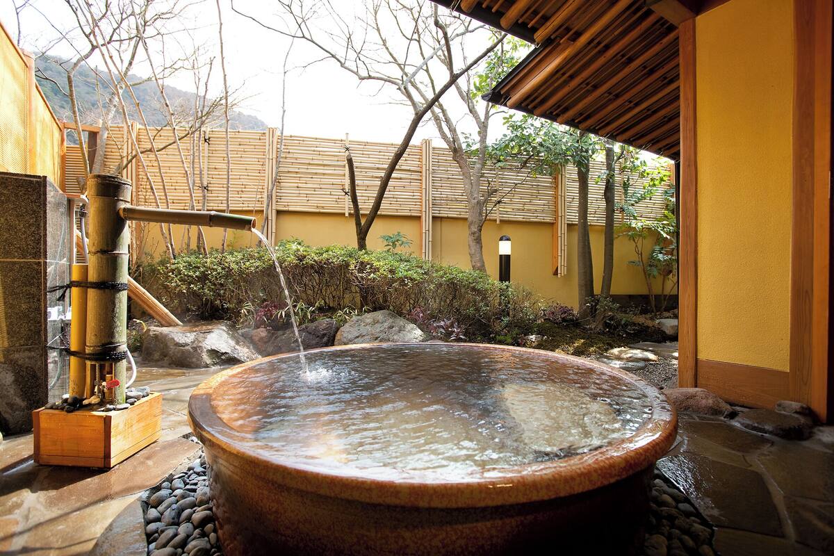 A traditional Japanese onsen with a stone hot spring, bamboo fence, and a wooden structure.