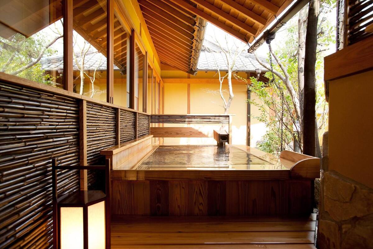 A traditional Japanese-style room with tatami flooring, a wooden bench, and a stone wall.