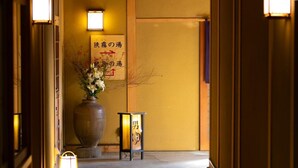 A hallway with traditional Japanese decor, including a large vase with flowers and a sign with Japanese characters. - Yufuin Santokan (Yufu)
