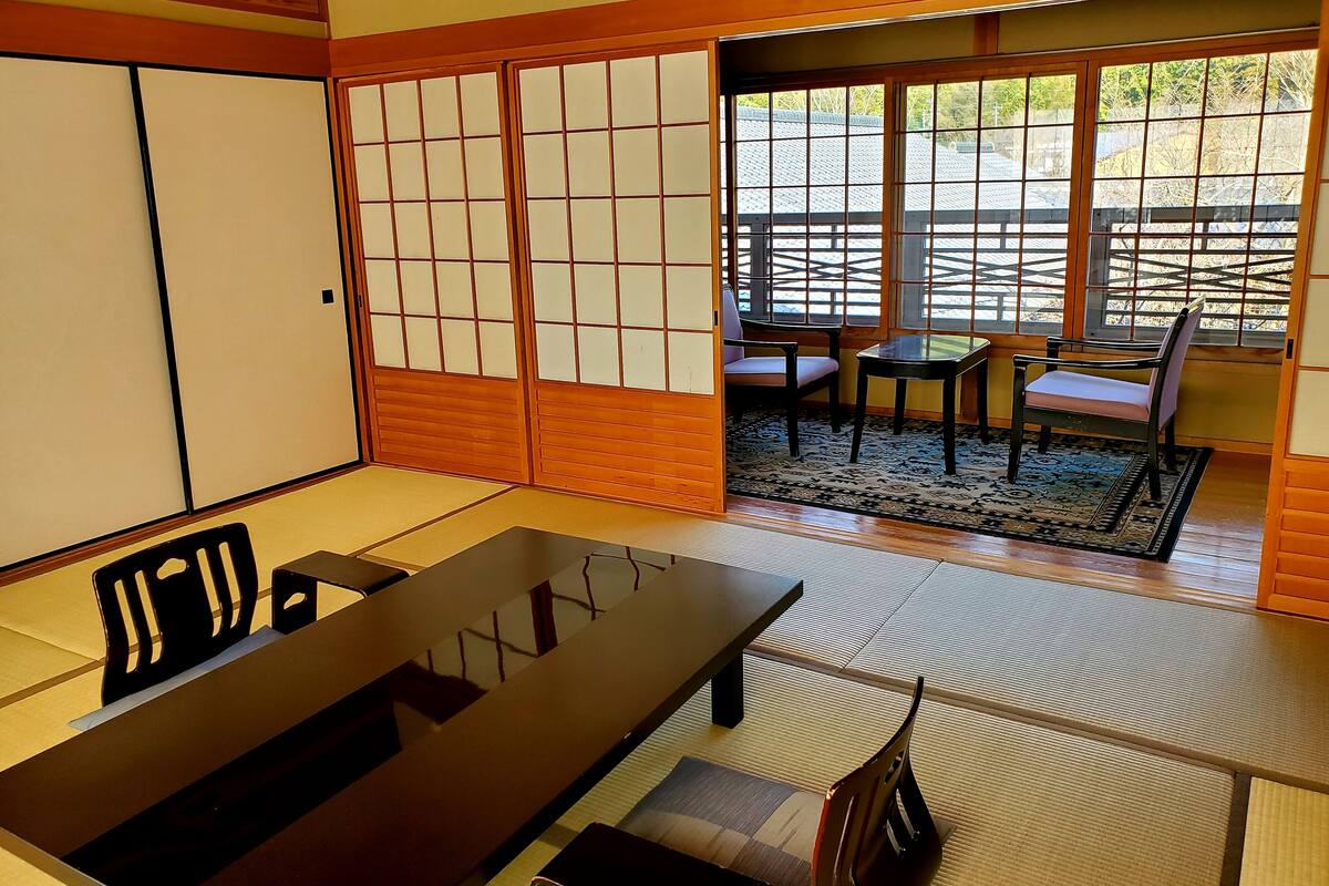 A traditional Japanese room with tatami flooring, a sliding shoji door, and a view of the outside through a window.