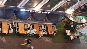 Un espace extérieur aménagé avec des tables et des chaises en bois, et une enseigne indiquant « Grill & Bar ».