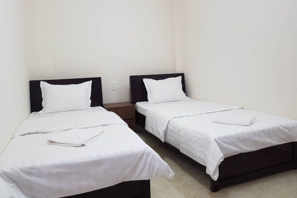 Une chambre avec deux lits simples, chacun doté d’une tête de lit en bois et de linge de lit blanc.