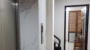 Un couloir avec un mur en marbre, une porte dotée d’un écran numérique, un escalier et, au fond, une porte en bois.