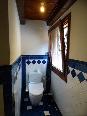A small bathroom with a toilet, a window with blinds, and a tiled floor.