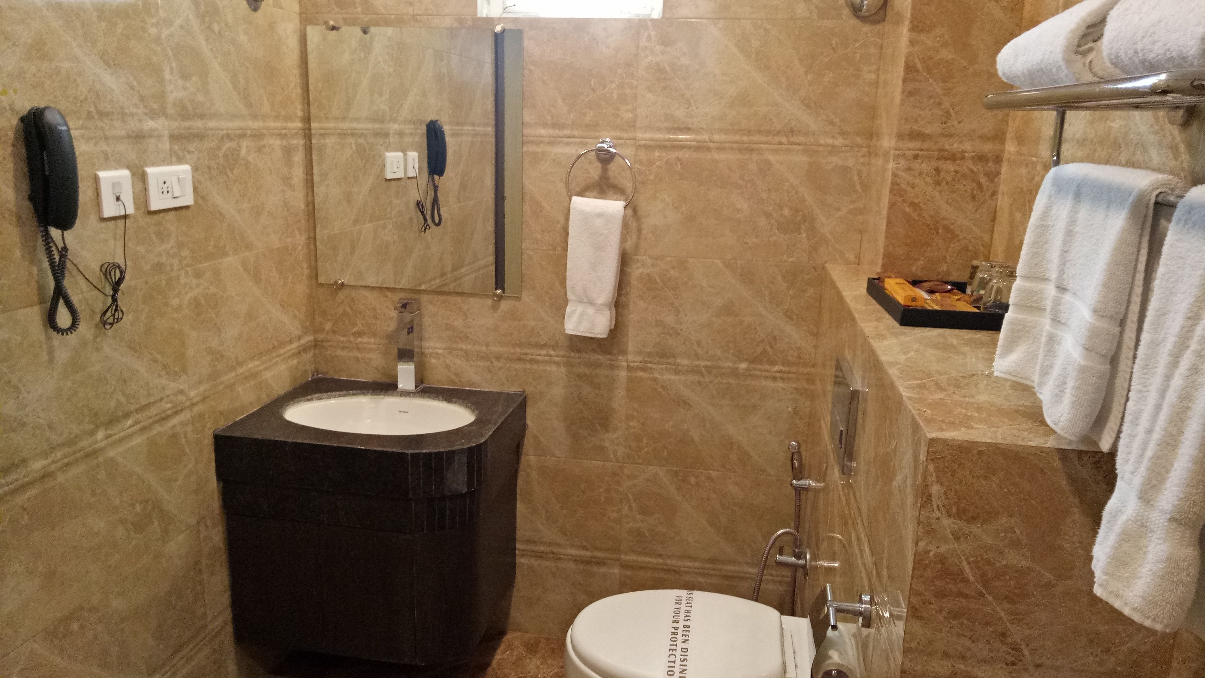 A bathroom with a sink, toilet, and shower. There is a telephone and a towel rack.