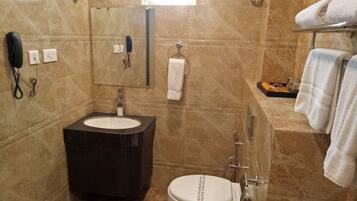 A bathroom with a sink, toilet, and shower. There is a telephone and a towel rack.
