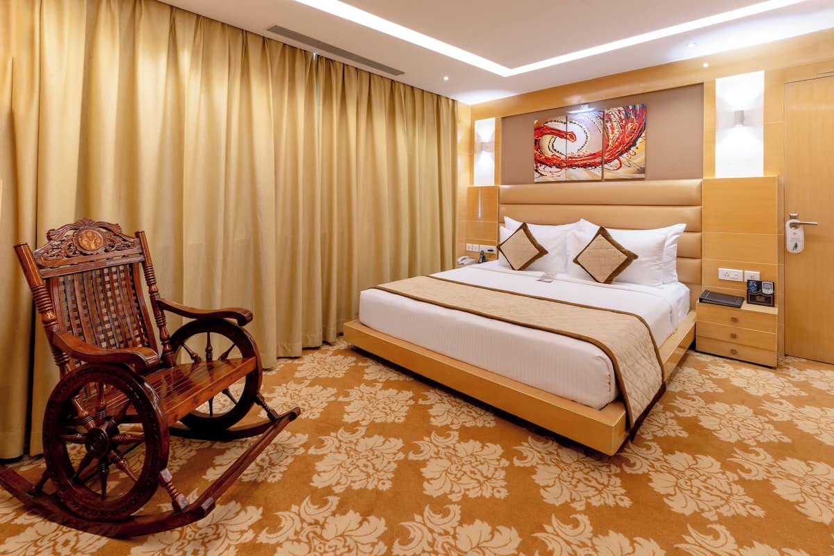 Habitación de hotel con una cama grande, un sillón mecedora, cabecera con detalles artísticos y alfombra estampada.