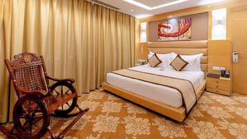 Habitación de hotel con una cama grande, un sillón mecedora, cabecera con detalles artísticos y alfombra estampada.