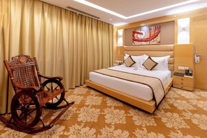 Habitación de hotel con una cama grande, un sillón mecedora, cabecera con detalles artísticos y alfombra estampada.