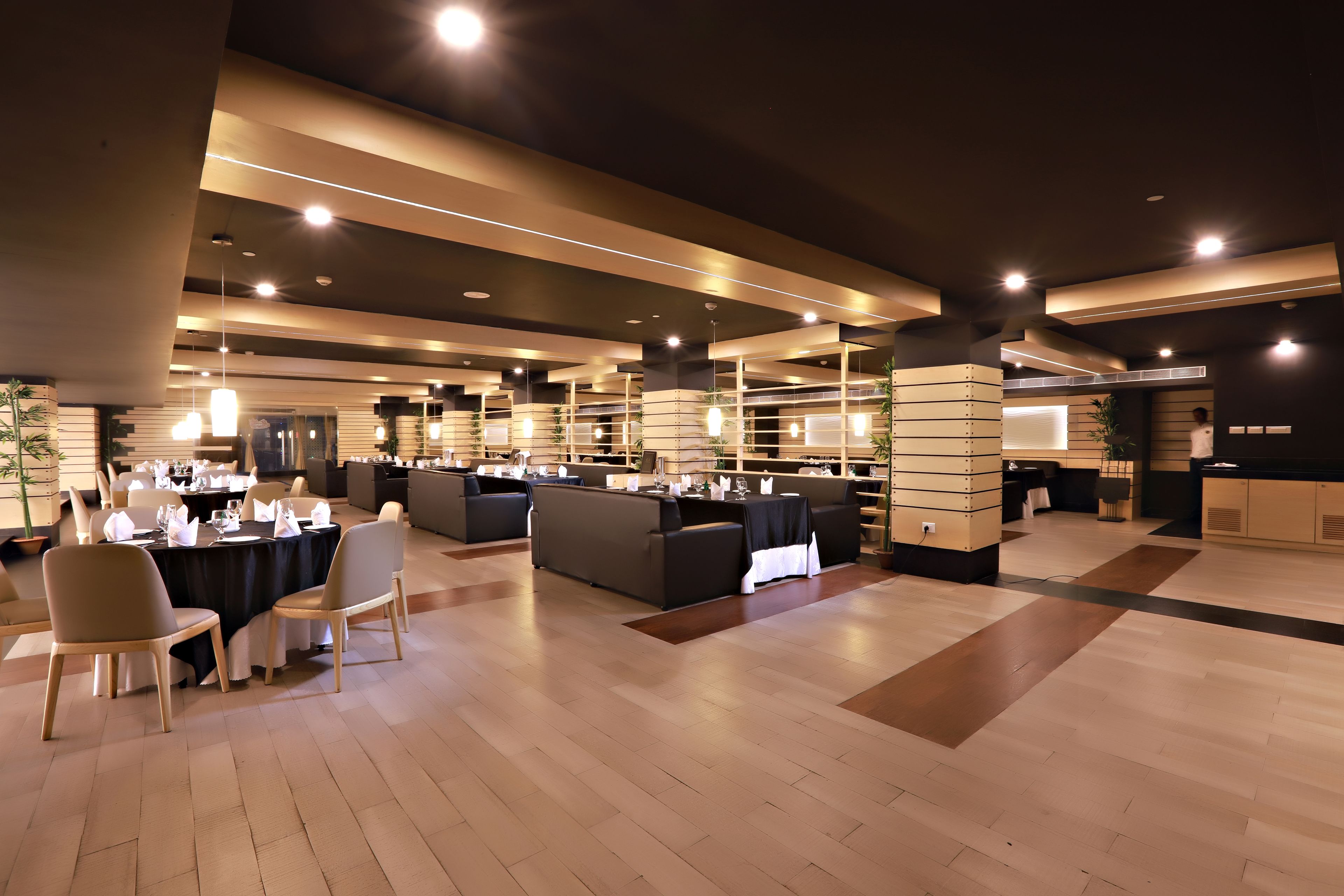 Un comedor moderno con varias mesas y sillas, una zona de bar y un mostrador de recepción.