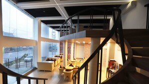 Un interior moderno con una escalera de caracol, zona de estar con mesas y ventanas amplias que ofrecen vistas al exterior.