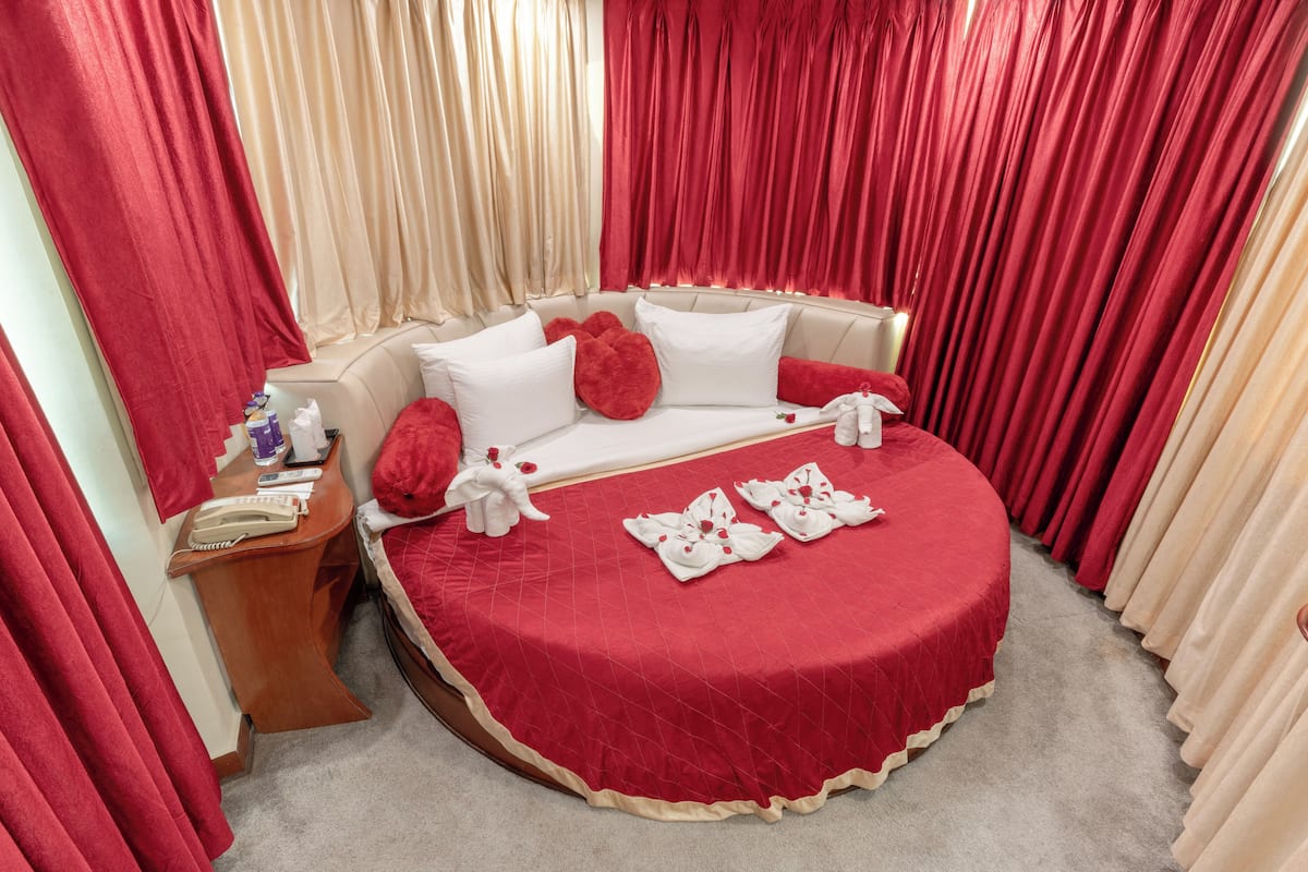 Una habitación de hotel con una colcha roja, almohadas blancas y cortinas rojas.