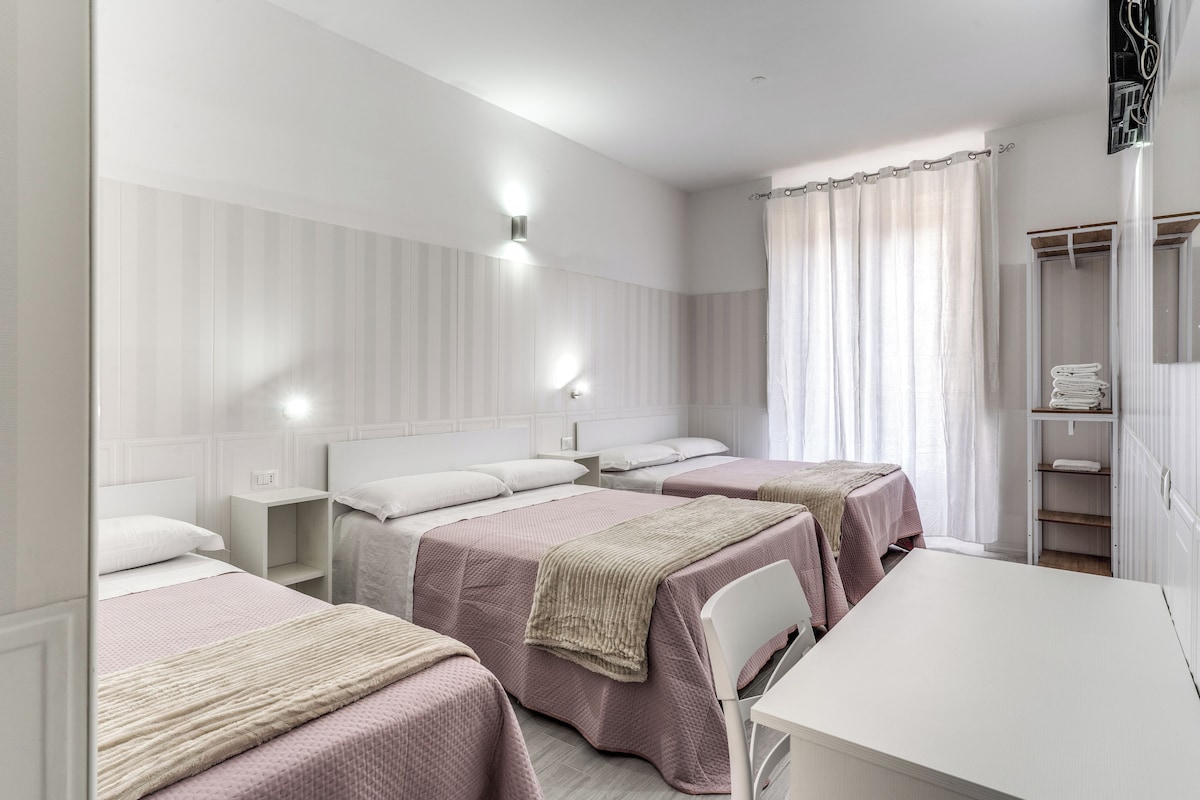 A hotel room with three beds, a white desk, and a wardrobe.