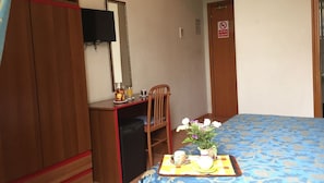 Ein Schlafzimmer mit Bett, Schreibtisch mit Stuhl, Wandfernseher und einer Tür mit Rauchverbot-Hinweis.