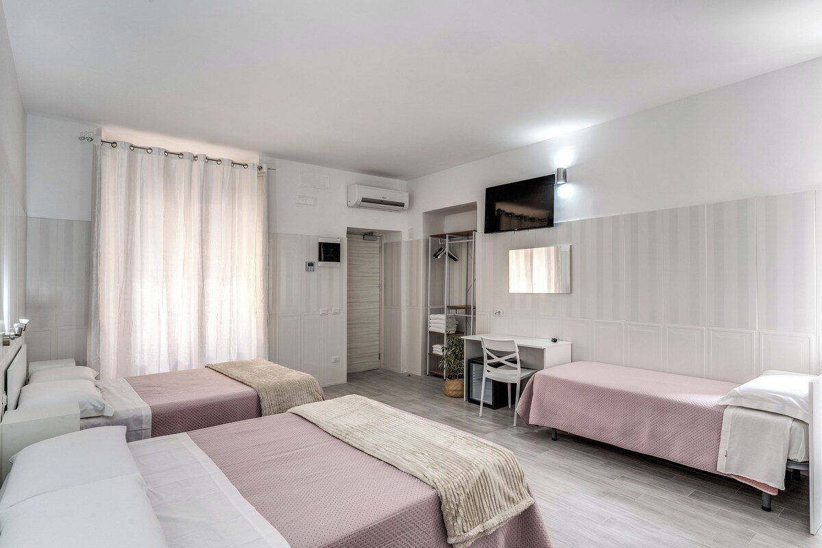 A hotel room with two single beds, a desk, a chair, a wardrobe, and a shower area.