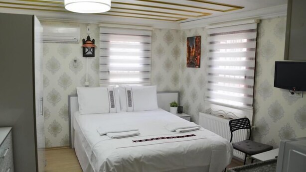 A bedroom with a bed, a desk, a chair, a radiator, and a TV. - Sophia Studio Apartments (Istanbul)