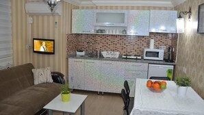 A compact living space with a kitchenette, a sofa, a small dining table with fruit, and a TV in the corner. - Sophia Studio Apartments (Istanbul)