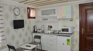 A compact kitchen with a microwave, kettle, and a small dining area with a chair and table.