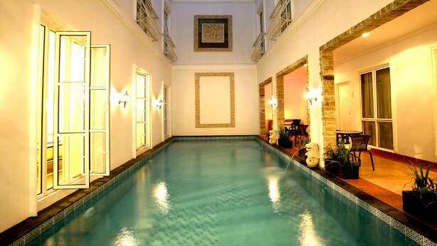 Una piscina con suelo de baldosas, rodeada de paredes con molduras decorativas y cuadros enmarcados.