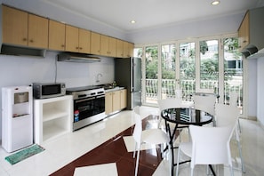 A modern kitchen with a dining area, large windows, and a view of greenery.