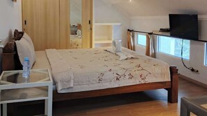 Un dormitorio con una cama, un televisor, un armario de madera y una mesita de noche con una botella de agua.