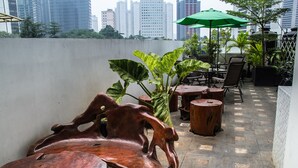Un espacio al aire libre con mobiliario de madera y un paraguas verde, con vistas a un paisaje urbano.