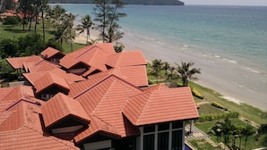 Ein Küstenhotel mit roten Ziegeldächern, Blick auf den Strand und einem Bergpanorama.