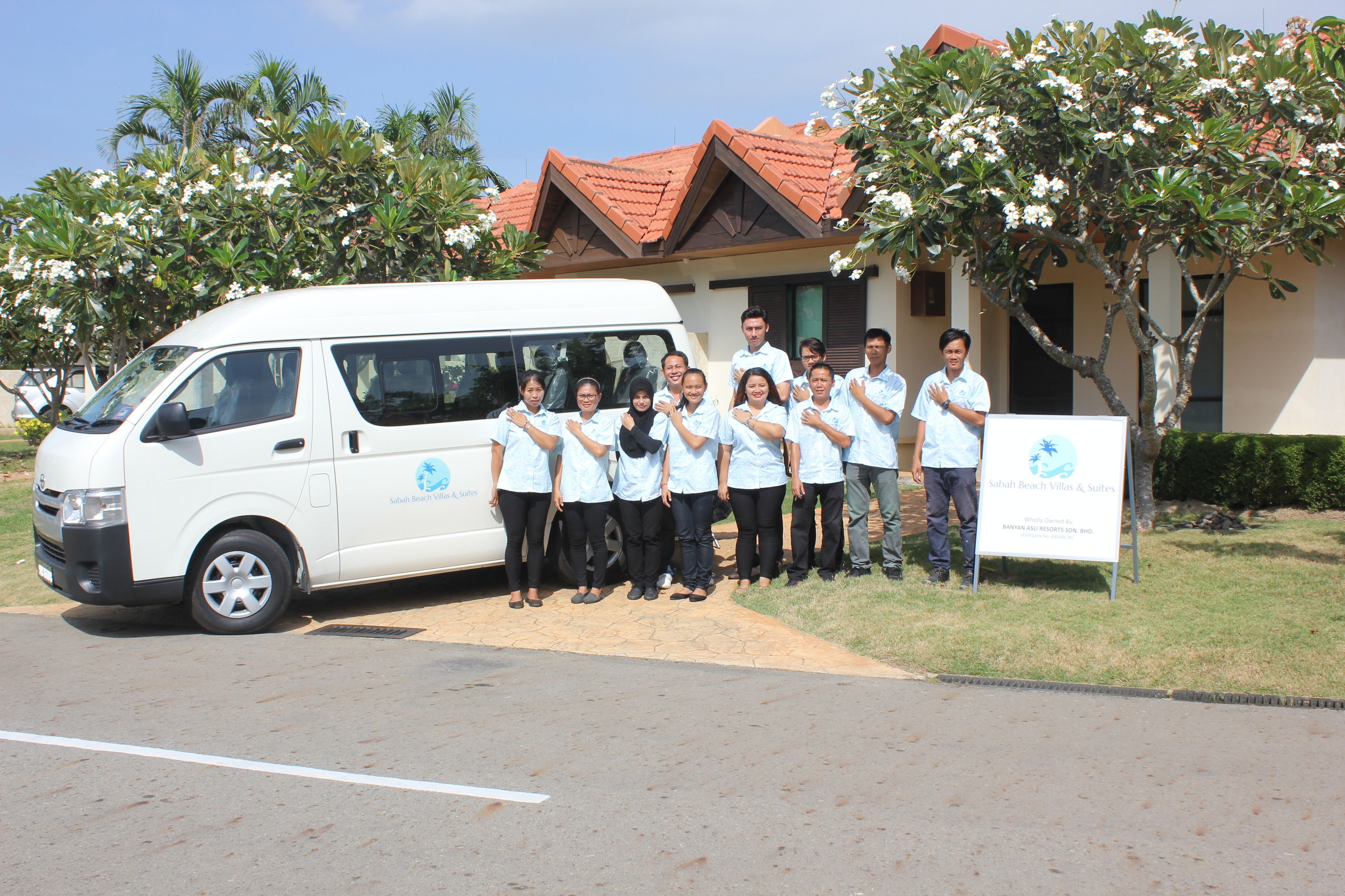 A group of people standing in front of a white van and a building with a red roof.