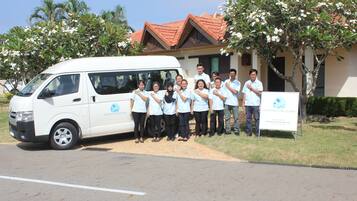 A group of people standing in front of a white van and a building with a red roof.
