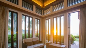 Ein großzügiges Wohnzimmer mit Sofa, Sesseln und Couchtisch. Große Fenster bieten Blick ins Freie.