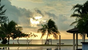 Ein ruhiger Poolbereich mit Blick auf den Sonnenuntergang über dem Meer, umgeben von Palmen und einer Laube.