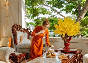 A room with a large ornate mirror, a sofa, a table with food and drinks, and a vase with yellow flowers. - Riverside Hotel (Dong Thuan)