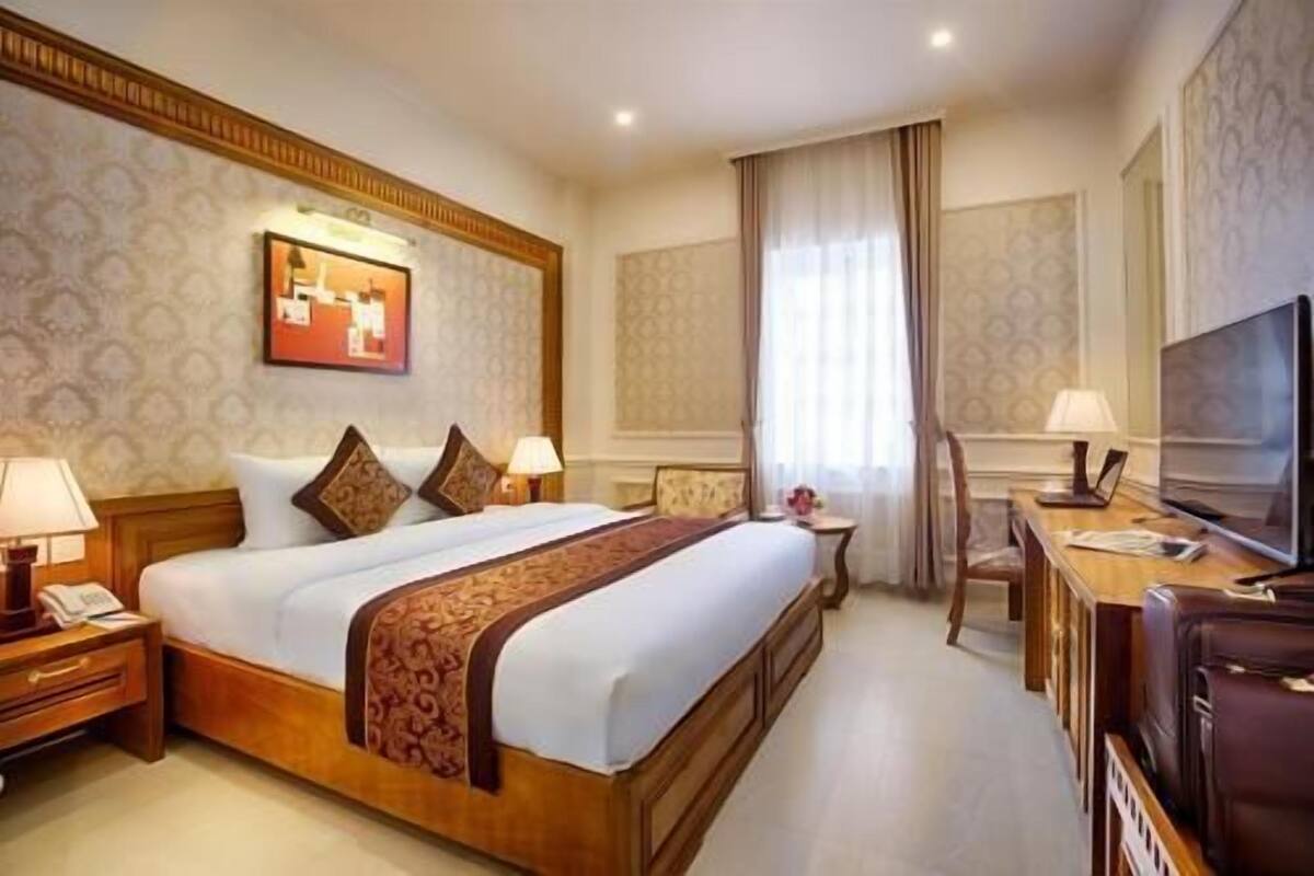 Habitación de hotel con una cama grande, mesitas de noche, un escritorio, una silla, un televisor y una ventana con cortinas.