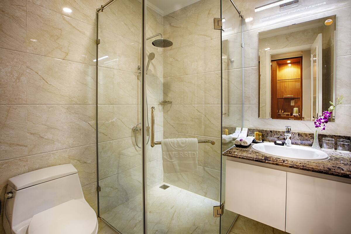 Un baño moderno con ducha de vidrio, inodoro blanco, encimera de mármol y lavamanos con espejo.