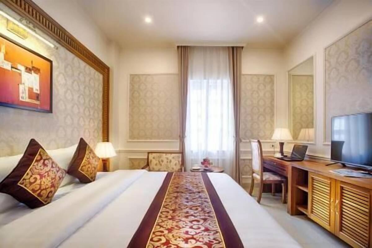Una habitación de hotel con una cama grande, un escritorio con una computadora portátil, un televisor y una ventana con cortinas.