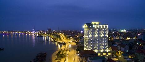 A high-rise hotel with multiple floors, a waterfront view, and a well-lit street adjacent to the building.