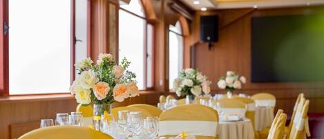 Ein Festsaal mit runden Tischen, gedeckt für eine festliche Veranstaltung, mit floralen Tischdekorationen und gelben Stuhlbändern.