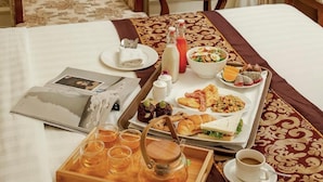 Una camera d'albergo con un letto, un tavolo imbandito per la colazione, un vaso di fiori e vista sul mare.